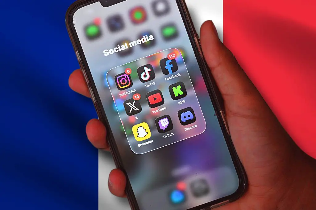 A hand holds a mobile phone showing a social media screen with the French flag in the background. (Photo by Saeed KHAN / AFP via Getty Images)