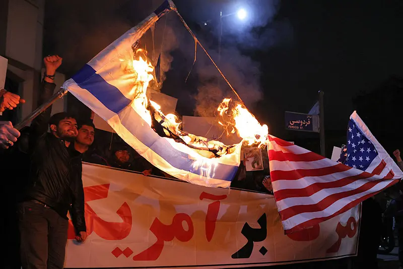Members of the Basij volunteer Islamic militia burn US and Israeli flags during a protest in front of the British Embassy in Tehran on January 14, 2026. (Photo by ATTA KENARE / AFP via Getty Images)